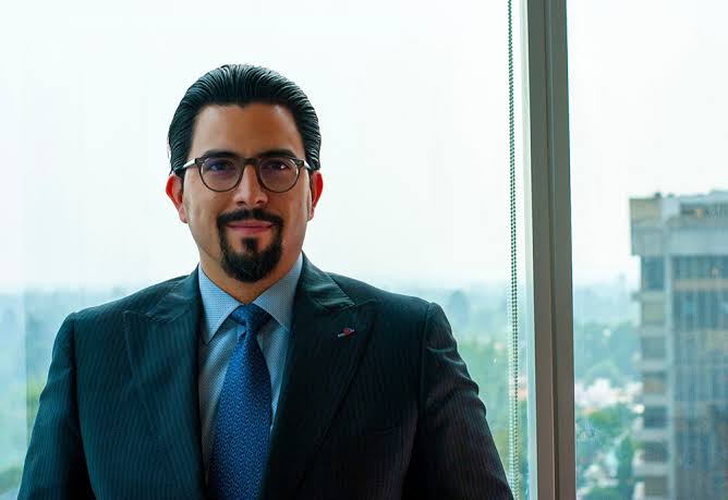 Fotografía de Adalberto Méndez  vistiendo un traje y corbata azul, usa lentes y barba. 